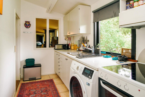 Cocina luminosa con electrodomésticos modernos, lavadora y ventana grande en casa vacacional en Holbæk, Dinamarca.