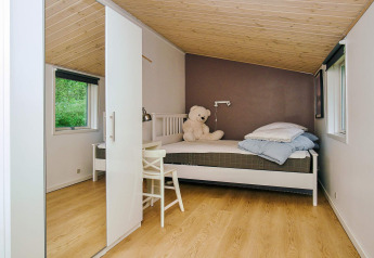 Acogedor dormitorio en la casa de vacaciones para 8 personas en Holbæk, Dinamarca, con cama, ventanas y oso.