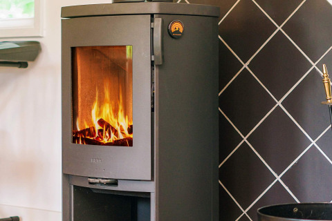 Moderne brændeovn med synlig ild i en hytte i Holbæk, Danmark, perfekt til vinterhygge.