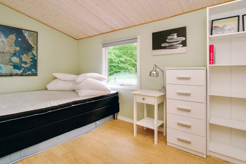 Heldere slaapkamer met eenpersoonsbed, bureau en ladekast, uitkijkend op groen bij een Deense lodge.