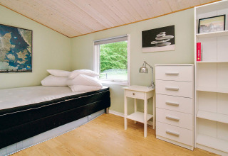 Heldere slaapkamer met eenpersoonsbed, bureau en ladekast, uitkijkend op groen bij een Deense lodge.