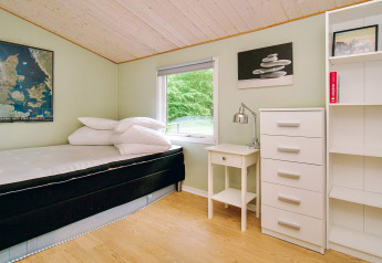 Helles Schlafzimmer mit Einzelbett, Schreibtisch, Kommode und Fenster mit Blick ins Grüne im Ferienhaus.