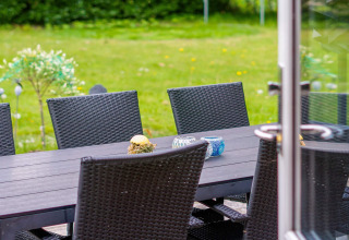 Buiteneettafel met zwarte wicker stoelen en decoraties, zicht op het gazon vanuit het terras.