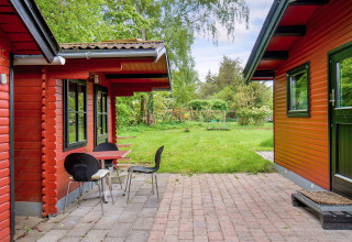 Udendørs terrasse ved 8-personers feriehus i Holbæk, Danmark, med røde træbygninger og grøn have.