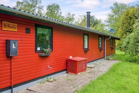 Casa de vacaciones roja llamada 'La Familia' con jardín y camino de piedra en Holbæk, Dinamarca.