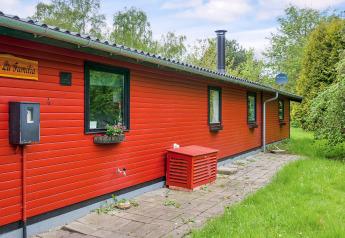 Rood houten vakantiehuis 'La Familia' met tuin en tegelpad, gefotografeerd in Holbæk, Denemarken.