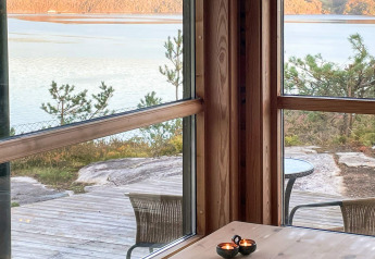 Blick aus einem Ferienhaus in Hjelmeland, Dänemark, mit großen Fenstern, See und Bäumen draußen.