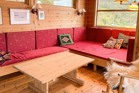 Gemütliche Sitzecke mit roten Polstern, Holztisch und Fenster im 7-Personen-Ferienhaus in Hjelmeland, Dänemark.