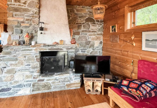 Soggiorno accogliente di una casa vacanze con camino in pietra, TV, divano rosso e pavimento in legno a Hjelmeland, Danimarca.