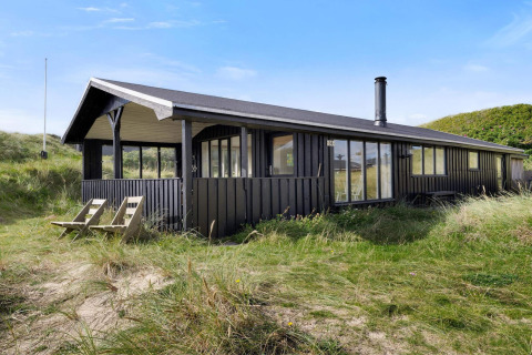 Casa sulla spiaggia in legno a Lokken, Danimarca, immersa tra dune sabbiose e erba sotto cielo azzurro.