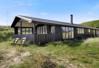 Strandhaus mit dunkler Holzfassade in Lokken, Dänemark, inmitten von Dünen bei sonnigem Wetter.
