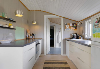 Cuisine moderne dans une maison de plage à Lokken, Danemark, avec armoires blanches et décoration chaleureuse.