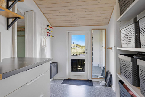 Eingangsbereich eines Strandhauses in Lokken, Dänemark, mit heller Einrichtung, Regalen und Spiegel.