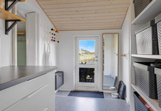 Inkomhal van een strandhuis in Lokken, Denemarken, met lichte aankleding, bakken en een spiegel.