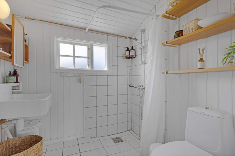 Baño luminoso y minimalista con ducha, inodoro y estanterías en casa de playa en Lokken, Dinamarca.