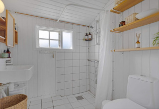 Salle de bain lumineuse, minimaliste avec douche, WC, étagères dans maison de plage à Lokken, Danemark.