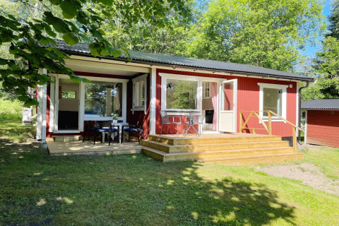 Accogliente baita rossa sul lago a Sollentuna con veranda in legno, tavolo all’aperto e alberi verdi intorno.