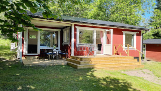 Gemütliche rote Hütte am See in Sollentuna mit Terrasse, Sitzbereich im Freien und viel grüner Natur.