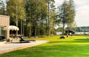 Udendørs terrasse med liggestole og parasol ved 4-stjernet feriehytte i Hestra, Sverige, tæt på sø og skov.