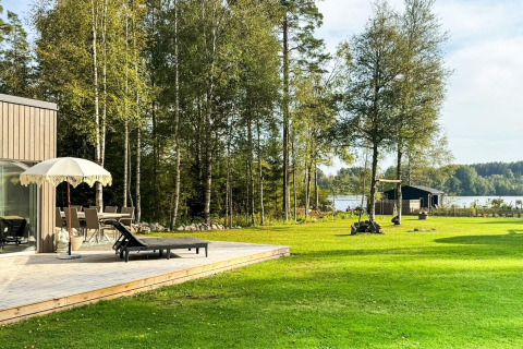 Terras met ligzetels en parasol aan een 4-sterren vakantiehuis in Hestra, Zweden, vlakbij meer en bomen.