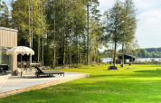 Udendørs terrasse med liggestole og parasol ved 4-stjernet feriehytte i Hestra, Sverige, tæt på sø og skov.