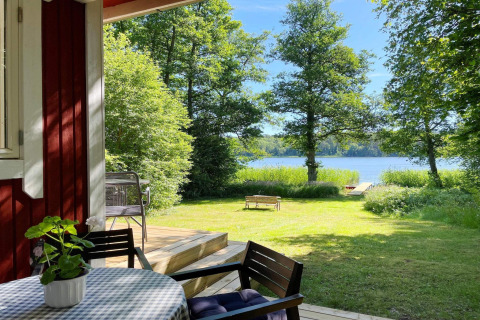 Vista desde la terraza de Lakeside Cabin Retreat en Sollentuna, Suecia, con lago, árboles y césped soleado.