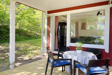 Veranda in legno con tavolo e sedie davanti a una cabina rossa sul lago a Sollentuna, Svezia, immersa nel verde.