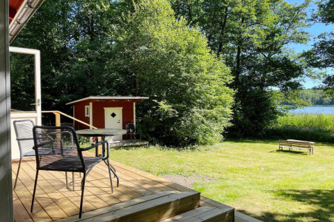 Terrazza in legno con tavolo e sedie, vista su giardino, casetta rossa, panchina e lago a Sollentuna, Svezia.