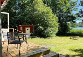 Wooden deck with table and chairs, garden view, red shed, bench, and lake at Sollentuna, Sweden.