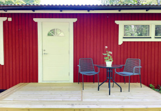 Rød og hvid hytte med lille træterrasse, to stole, et bord og en plante, Sollentuna, Sverige.