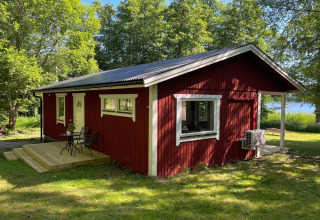 Casetta rossa vicino al lago con veranda, circondata da alberi verdi a Sollentuna, Svezia, in una giornata di sole.
