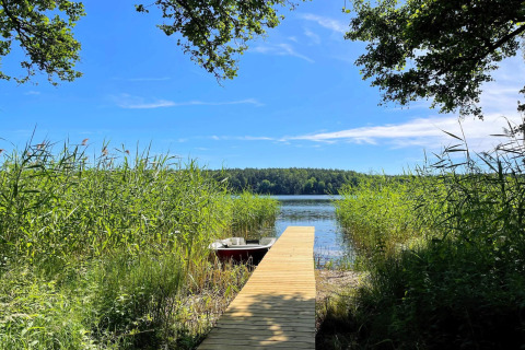 Muelle de madera junto a un lago en Lakeside Cabin Retreat en Sollentuna, Suecia, rodeado de vegetación verde.