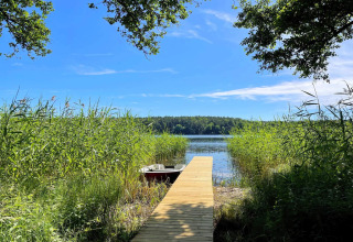 Muelle de madera junto a un lago en Lakeside Cabin Retreat en Sollentuna, Suecia, rodeado de vegetación verde.