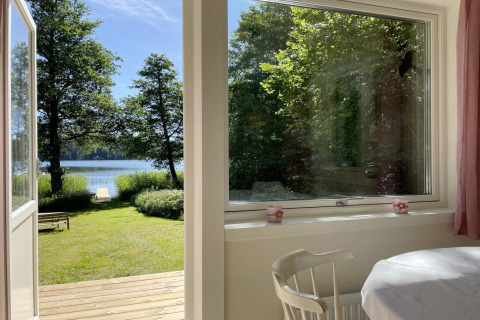 Udsigt fra en hytte ved søen i Sollentuna, Sverige, med åben dør, træterrasse og grøn have.