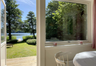 Blick aus einer Hütte am See in Sollentuna, Schweden, mit offenem Türrahmen und grünem Garten.