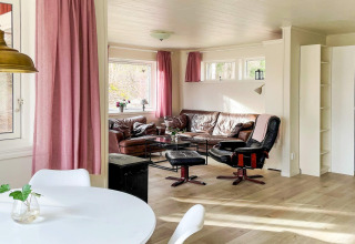 Gemütliches Wohnzimmer in einer Hütte in Schweden mit rosa Vorhängen, Ledersofa und viel natürlichem Licht.