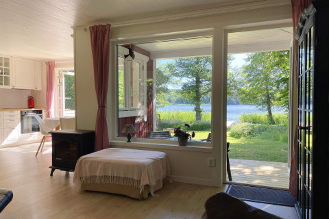 Cozy living room in a lakeside cabin retreat in Sollentuna, Sweden, with large windows overlooking a lake.