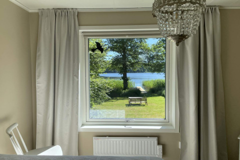 Bedroom window overlooking a lake and bench at the Lakeside Cabin Retreat in Sollentuna, Sweden on a sunny day.