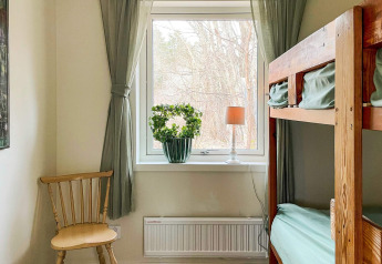 Chambre lumineuse avec lits superposés, rideaux verts, chaise en bois et plante près de la fenêtre.