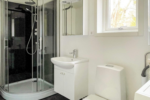 Modern bathroom with shower, white sink, toilet, and window at Lakeside Cabin Retreat in Sollentuna, Sweden.
