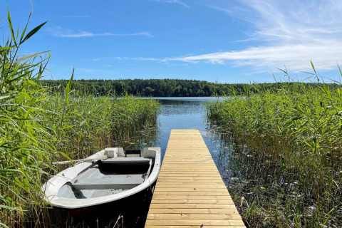 A wooden dock at Lakeside Cabin Retreat in Sollentuna, Sweden, with a rowboat among reeds and lake view.