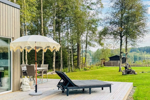 Buitenterras bij een vakantiehuis in Hestra, Zweden, met ligstoelen, parasol en uitzicht op het meer.