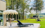 Terraza exterior en una casa de vacaciones en Hestra, Suecia, con tumbonas, sombrilla y vista al lago.