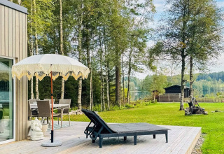 Udendørs terrasse ved et feriehus i Hestra, Sverige, med liggestole, parasol og udsigt over søen.