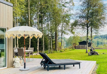 Terraza exterior en una casa de vacaciones en Hestra, Suecia, con tumbonas, sombrilla y vista al lago.