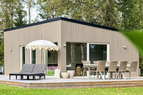 Moderne feriebolig i Hestra, Sverige, med træfacade, stor terrasse, liggestole og spisebord udendørs.