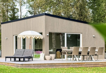 Modernes Ferienhaus in Hestra, Schweden, mit Holzfassade, großer Terrasse, Sonnenliegen und Esstisch.