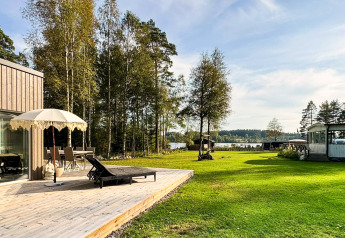 Træterrasse med parasol og liggestol ved feriehus nær Hestra, Sverige, grøn have og udsigt til søen.