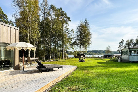 Houten terras met parasol aan viersterren vakantiewoning in Hestra, Zweden, met tuin en zicht op het meer.