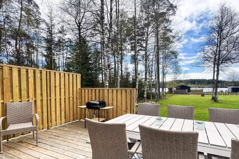 Terrasse mit Esstisch, Stühlen und Grill, umgeben von Natur und Seeblick bei Hestra, Schweden.